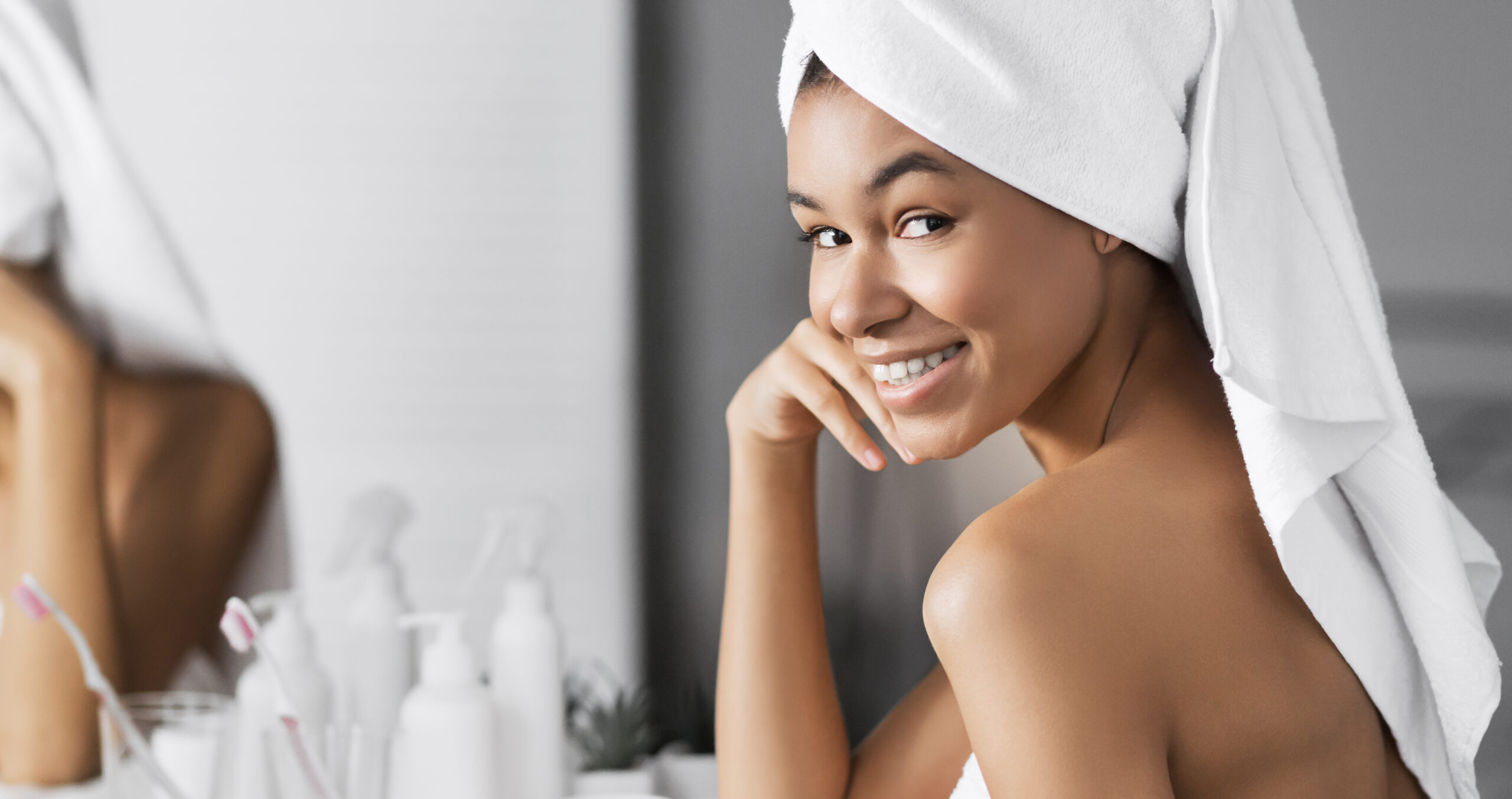 Woman with hair wrapped in towel, smiling over shoulder